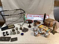 Photo showing many of the antique and vintage items including wire basket, Fire Alarm Signal sign, green glass bottle, brass item, door knobs, salt & pepper shakers, small basket and more.