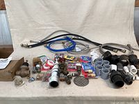 View of full lot showing all hoses, boxed valve, various fittings, spigots, and pipes arranged on a beige cloth backdrop.