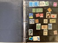 View of one binder page with assorted vintage U.S. postage stamps in various colors and denominations, placed in black plastic sleeves