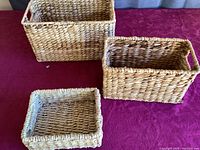 Three blonde woven nesting baskets in varying sizes arranged on a red surface.