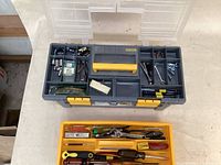 Closed toolbox top with visible compartment containing small hardware and tools, yellow handle and latch, gray body
