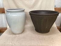 Front view of both planters side by side on cloth background, white ceramic on left, brown plastic on right.