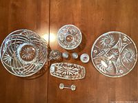 Top view of collection showing all crystal and glass items including large bowls, plates, oil and vinegar holders, small bowls and a cutting tool rest, displayed on wood surface.