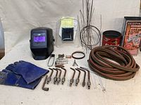 Full lot view showing welding helmet, gloves, copper torch tips, long hose, metal wire, and books