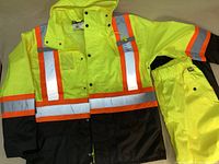 Photo of the front of the fluorescent yellow and black waterproof jacket with reflective stripes and elastic waist pants laid flat.