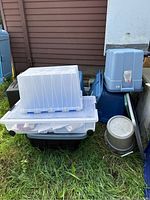 Photo of various storage bins stacked outside on grass showing different sizes, colors, and lid types.