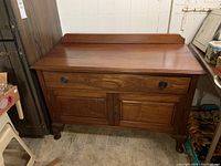 Front view of vintage wooden cabinet showing drawer and double doors with keyhole hardware