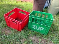 Two crates on grass: green 7-Up beverage crate with logo on the right, red milk crate on the left.
