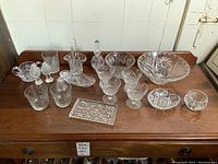 Wide view of entire crystal collection displayed on wood surface showing various bowls, dishes, glasses, and salt and pepper shakers.