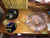 Five decorative glass dishes displayed on a wooden surface, the largest has dragonfly motifs and measures 15 inches across, smaller dishes include varying colors and designs.