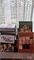 Photo showing stack of All in the Family TV series DVD volumes along with Golden Girls TV series DVDs in a box.