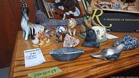 Group of assorted figurines including animals like lion, rabbit, bird, and a soap stone boat-shaped item on a wooden table