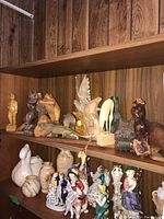 Wide view of two shelves with assorted wooden and porcelain figurines, showing variety in size and material.