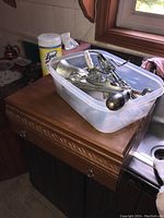 Wooden box on countertop with metal hand-crank meat grinder and hand mixer inside a plastic container.