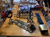 Wide view of the lot showing the two metal candle holders, a large cowbell, and two horse brasses on straps placed on a wooden table