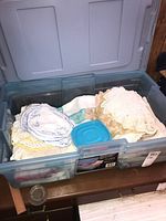Plastic storage box filled with folded linens including tablecloths and dollies.