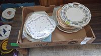 Top down view of two stacks of assorted plates with floral and patterned designs inside a cardboard box