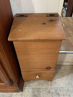 Front view of vintage wooden potato bin showing slanted top lid with iron hinges and small drawer at base with white knob.