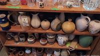 Wide shot of a wooden shelf displaying multiple pottery and ceramic vases with different shapes, colors, and sizes. Includes items from Huronia Pottery Ltd, Scheurich Keramik, and others.