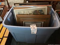 Bin filled with about 10 framed prints, seen from above, showing various frame styles and sizes