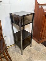 Full view of shelving unit showing chrome legs and three plastic shelves in a narrow vertical configuration.