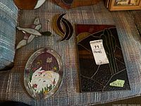 Group photo of stained glass pieces on fabric surface, showing cactus panel, duck shape, oval floral design, bird design, and abstract crescent shapes
