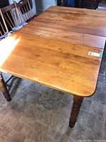 Full view of wood dining table with turned legs on tiled floor, chairs visible in background