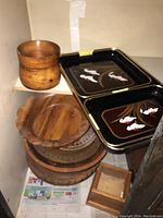 Wooden bowls and serving trays stacked inside a cabinet. There are multiple wooden trays and bowls, and two black plastic trays with fish designs.