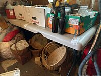 Photo showing the folding work table top with multiple boxes, bottles, and other items placed on it, also showing some baskets underneath the table.