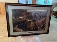 Framed art print sitting on a piece of furniture inside a home, showing the artwork landscape and frame.