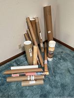 Group of cylindrical tubes with rolled posters and prints inside, arranged on floor near corner of room
