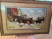 Full view of framed western art showing cowboys and horses on a dusty street outside a saloon and hotel.