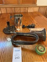 Overview of all lot items on wooden table: bugle, candlestick holder, tankard mug, telegraph key and aquarium food tin