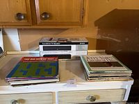 Photo showing two stacks of vinyl records and the boxed AccuVoice TV Speaker on a white cabinet.