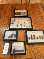 Overview of six framed displays containing metal relics and collectibles from 1800s-1900s, arranged on wooden surface.