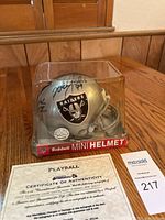 Front angle view of the silver Raiders mini helmet in display case with visible autographs and Certificate of Authenticity next to it.