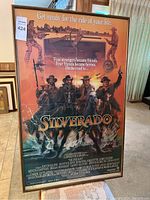 Framed Silverado movie poster featuring four cowboys on horseback with a background showing a sunset and a woman portrait. Movie credits and tagline visible.