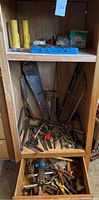 Wide view of entire wooden cabinet shelf with assorted hand tools and accessories inside.