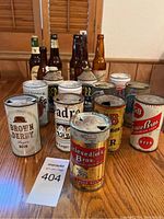 Photo showing the assortment of vintage beer cans, mostly rusty with pull tabs, placed on a wooden table with seller lot number visible