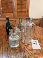 Front view of 13 vintage bottles on wood table showing variety in size, color, and closure types.