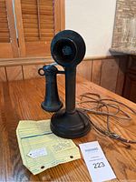 Full view of the vintage Kellogg candlestick telephone sitting on a wooden surface with attached cord, showing the entire item and original wiring.