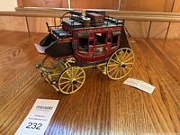 Full view of the Wells Fargo stagecoach model on a wooden floor, showing wheels, seats, luggage, and body detail.