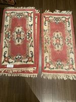 Two Chinese rose and cream coloured rugs side-by-side, showing size and design. Fringed edges visible.
