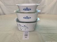 Three white casserole dishes stacked; two top with blue Cornflower pattern, bottom with purple Shadow Iris pattern