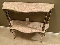 Front view showing two-tier cultured marble tops with scalloped edges and gold metal frame with ornate legs.