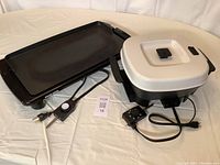 Electric griddle with 20 x 10 inch cooking surface next to an electric skillet with white lid, both Black & Decker brand, with power cords and temperature controls.