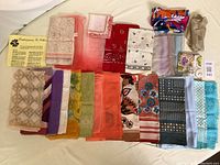 Assortment of 25 vintage ladies scarves laid out flat showing various colors and patterns including florals, geometrics, polka dots, and solids. Scarf fabrics vary including silk and other lighter materials. Includes a yellow instruction sheet on scarf tying ideas.