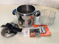 Pressure cooker pot, lid with locking handle, wire basket, and instruction manuals laid out on a flat surface