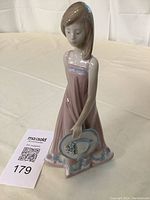 Full view of the porcelain figurine showing the girl wearing a pink dress and holding a blue and white hat with flowers.