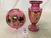 Pair of cranberry colored Bohemian glass vases with gold floral embellishments, one round and one pedestal shaped